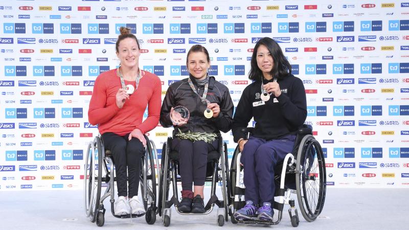 three female wheelchair racers on the podium with their medals
