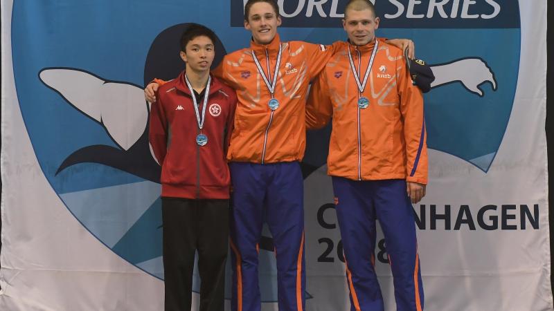 three male swimmers link arms on the podium