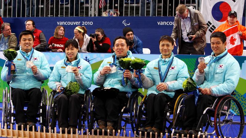a group of wheelchair curlers celebrate on the podium