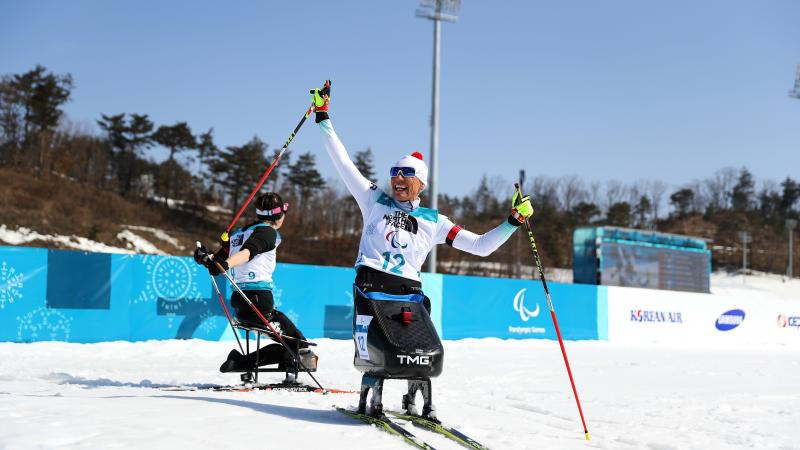a female Nordic sit skier celebrates on the finish line
