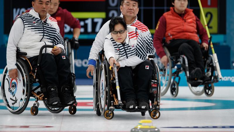 Woman in wheelchair playing curling with three people in wheelchairs observing
