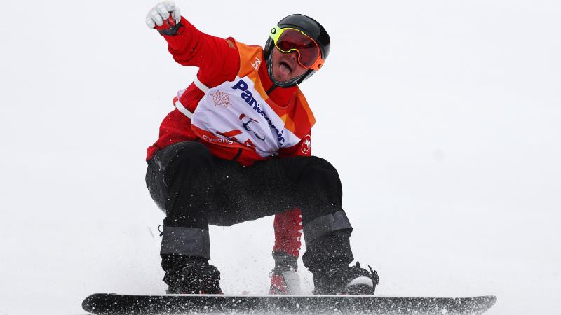 a male Para snowboarder sticks out his tongue at the end of his run