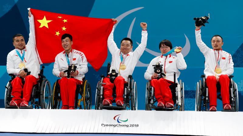 a team of wheelchair curlers hold up the Chinese flag with their medals