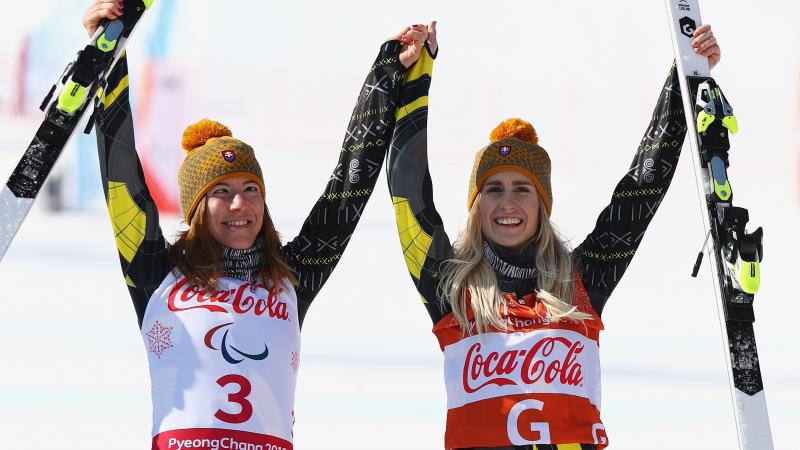a female vision impaired skier and her guide raise their arms in celebration