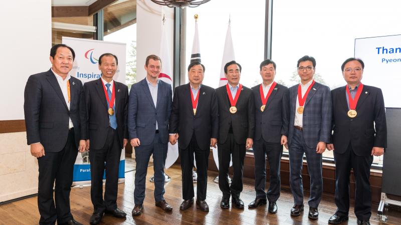 Eight men standing, six of them with the Paralympic Order medal 