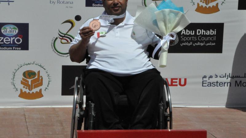 Man in wheelchair holding medal and flowers