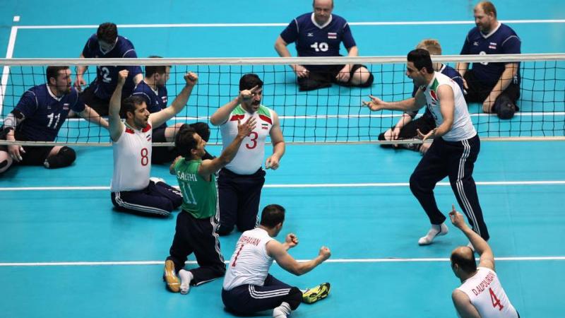 a group of male sitting volleyball players celebrate on the court