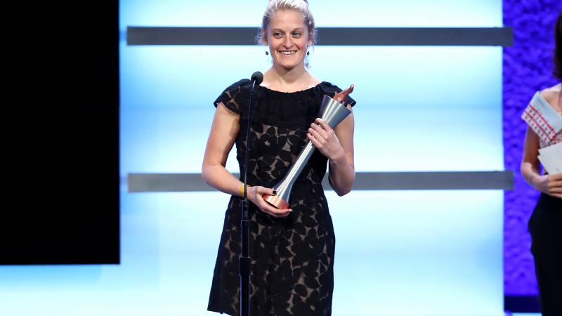a woman stands on stage holding a trophy