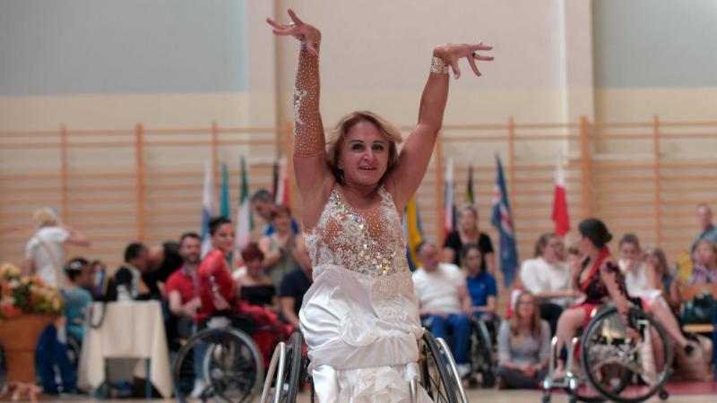 a female wheelchair dancer raises her arms above her head as part of a move