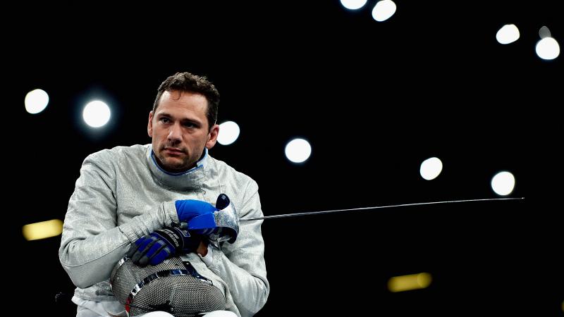 a male wheelchair fencer holding a foil and his helmet