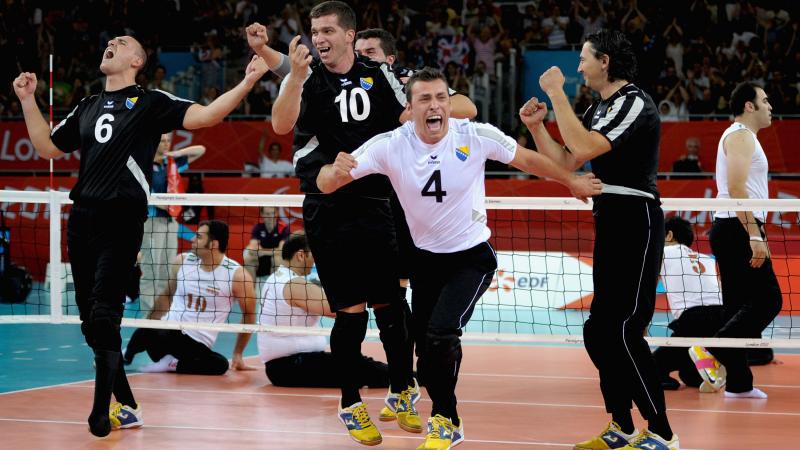 a group of male sitting volleyballers celebrate on the court