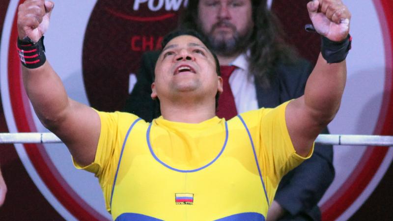 a male powerlifter raises his arms in celebration on the bench