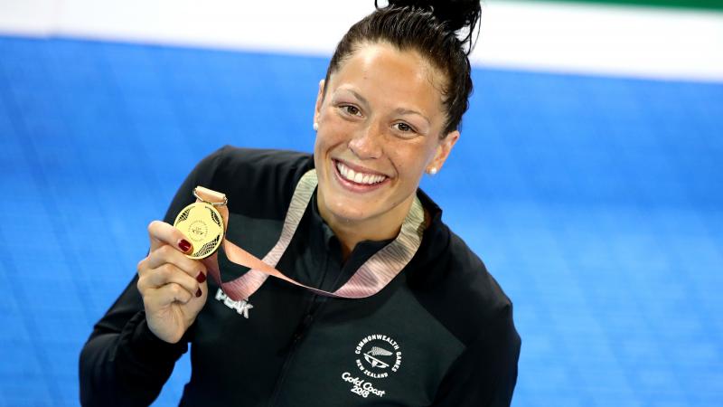 female Para swimmer Sophie Pascoe holds up a gold medal by the pool