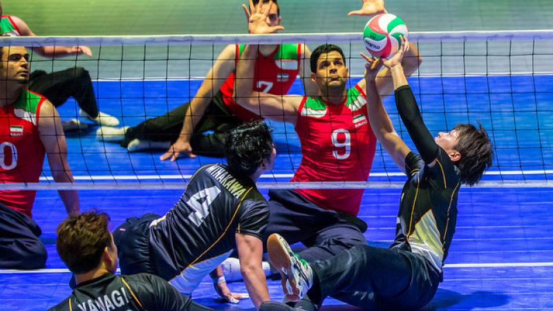 Japanese sitting volleyball player sets the ball while an Iranian athlete prepares to block