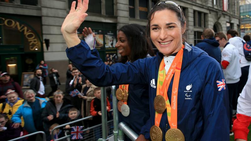 female Para cyclist Sarah Storey waves to fans from the top of a bus 
