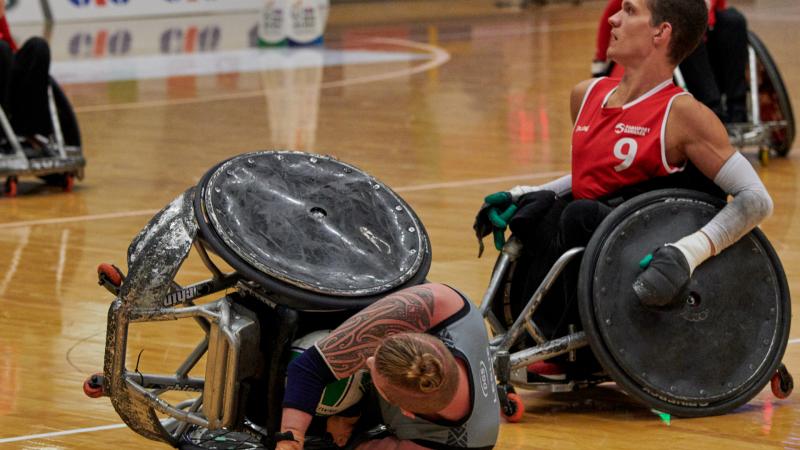 a Danish wheelchair rugby player on the ground after a tackle from a New Zealand wheelchair rugby player