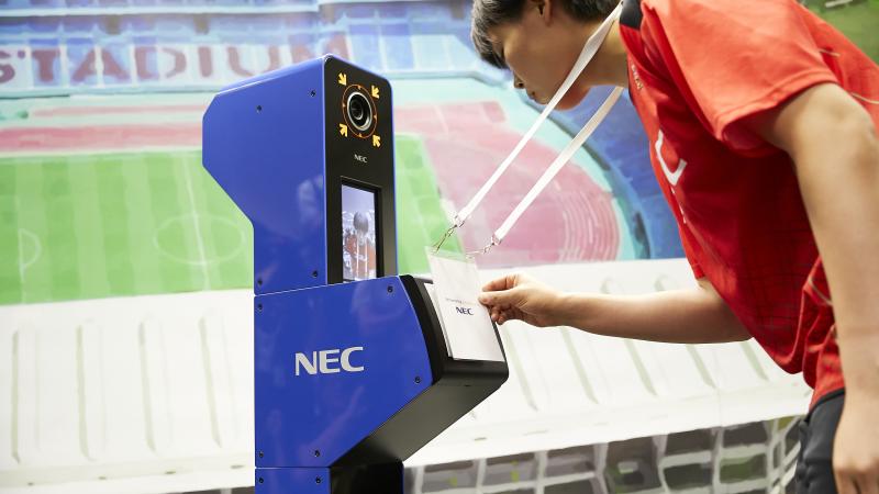 a person looks into a camera while displaying their accreditation in a simulation of the Tokyo 2020 system