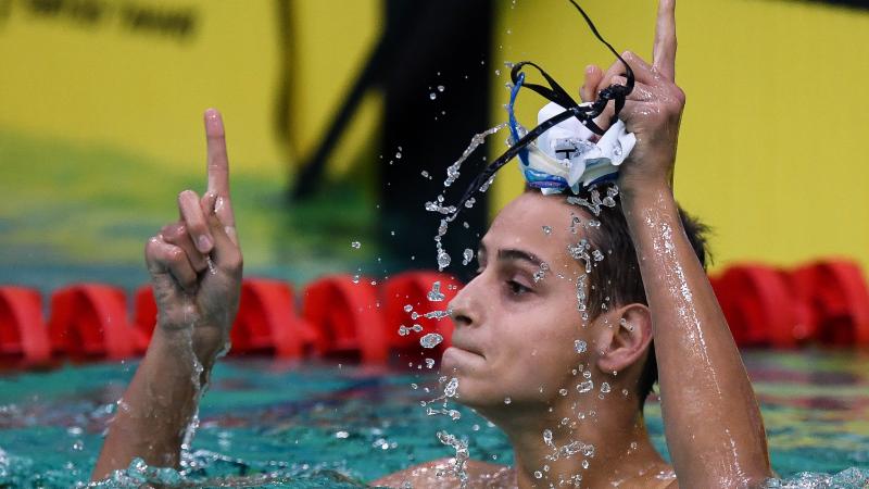 male Para swimmer Ugo Didier raises his fingers in celebration in the pool after winning his race