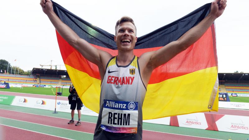 male long jumper Markus Rehm holding up the Germany flag and smiling