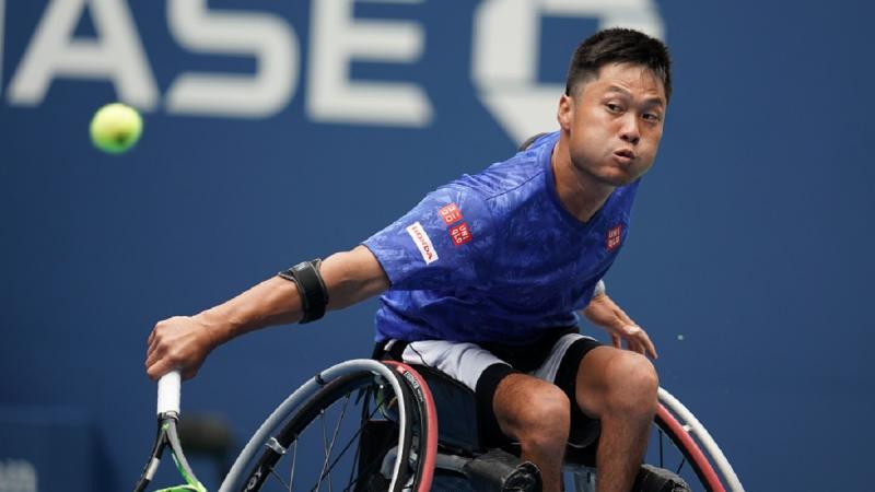 Japanese man in wheelchair reaches to his tennis ball