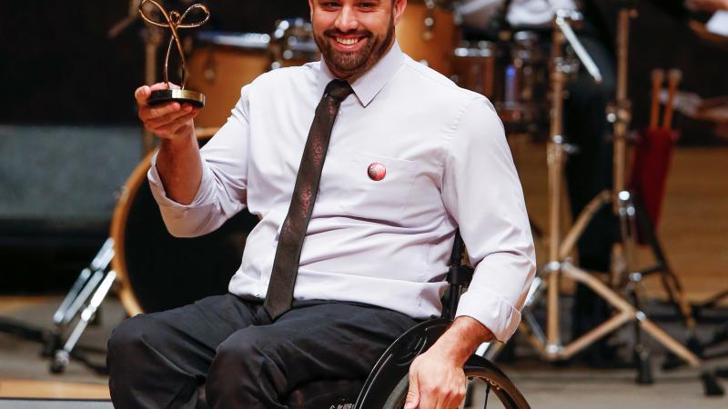 male wheelchair fencer Jovane Guissone holds up a trophy