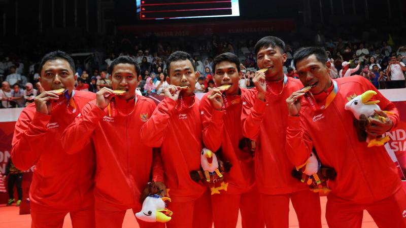 a group of Indonesian male Para badminton players biting their gold medals