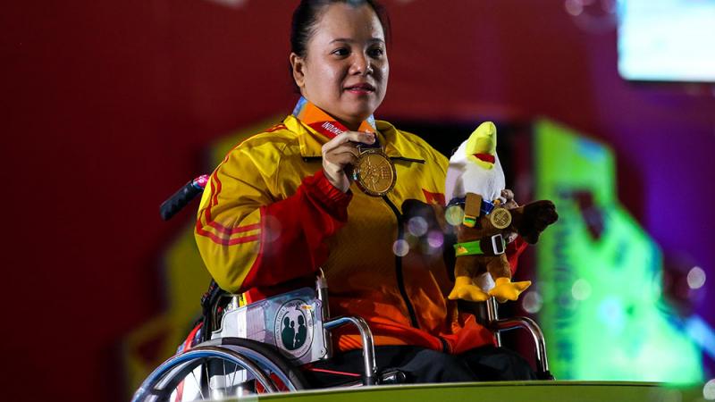 female powerlifter Dang Thi Linh Phuong on the podium holding up her gold medal