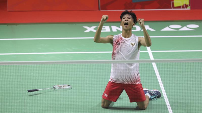 male Para badminton player Dheva Anrimusthi falls to his knees and clenches his fists on the court