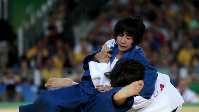 female judoka Li Liqing wrestles another female judoka to the ground on the mat