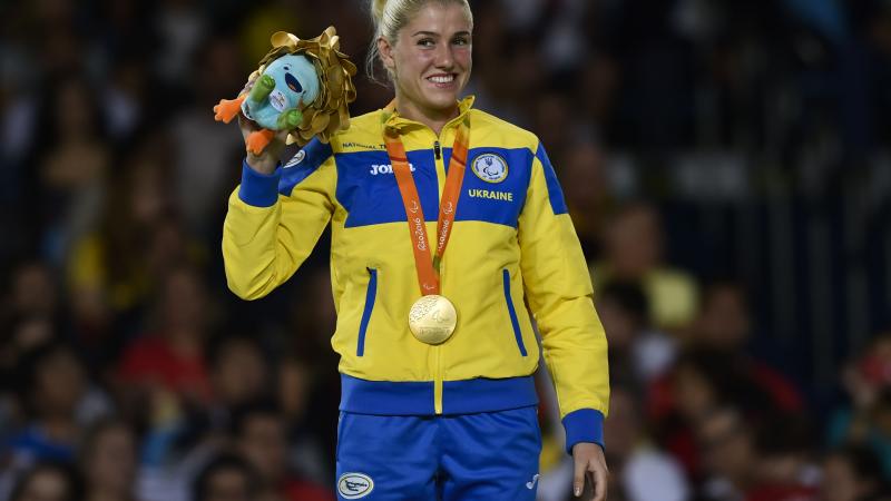 female judoka Inna Cherniak holds up a mascot teddy and her medal on the podium