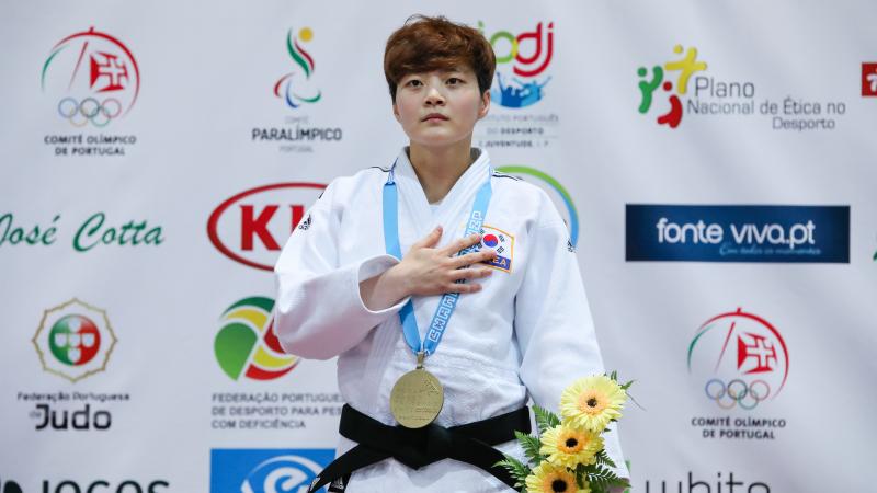 female judoka Soohee Choi holds her hand over her heart on the podium with a gold medal round her neck