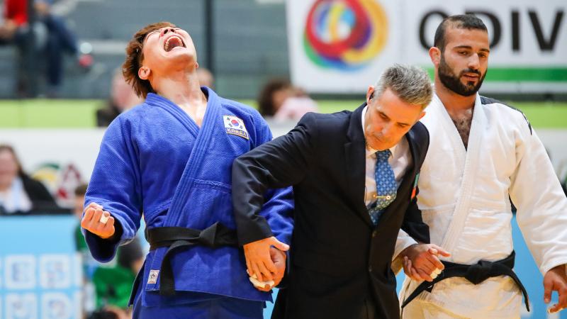 A men in suit holding the hands of two men in judo kimonos
