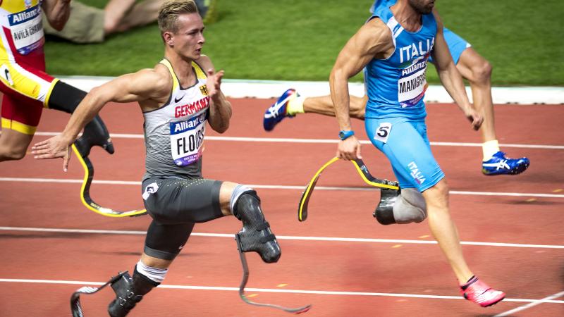 A man with prosthetic legs running against three competitors on an athletics' track