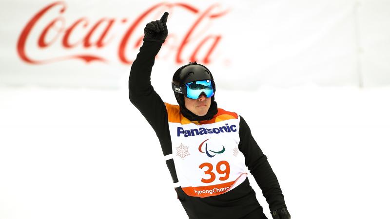 male Para snowboarder Matti Suur-Hamari raises his finger as he crosses the finish line