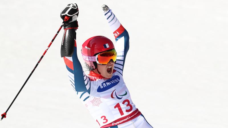 female Para alpine skier Marie Bochet raises her arms on the slopes after crossing the finish line