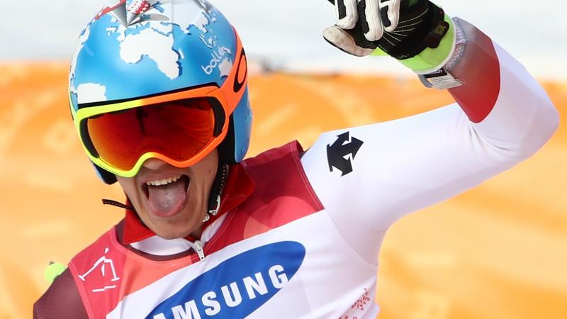 male Para alpine skiing Theo Gmur punches the air and smiles after crossing the finish line