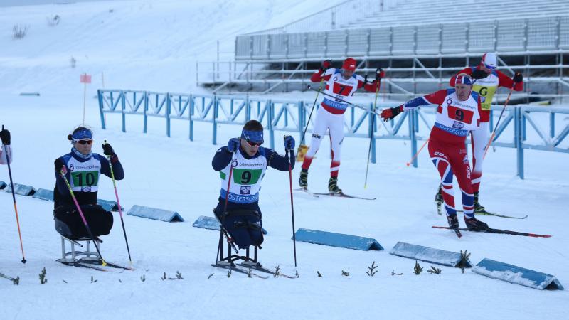 A group sitting and standing skiers competing in a Para biathlon race
