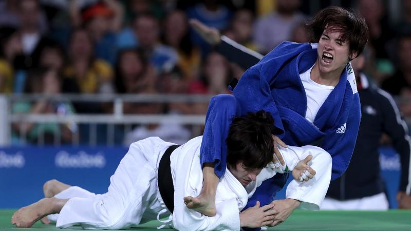 Female judoka Sandrine Martinet in a blue robe throws a judoka in a white robe onto the mat
