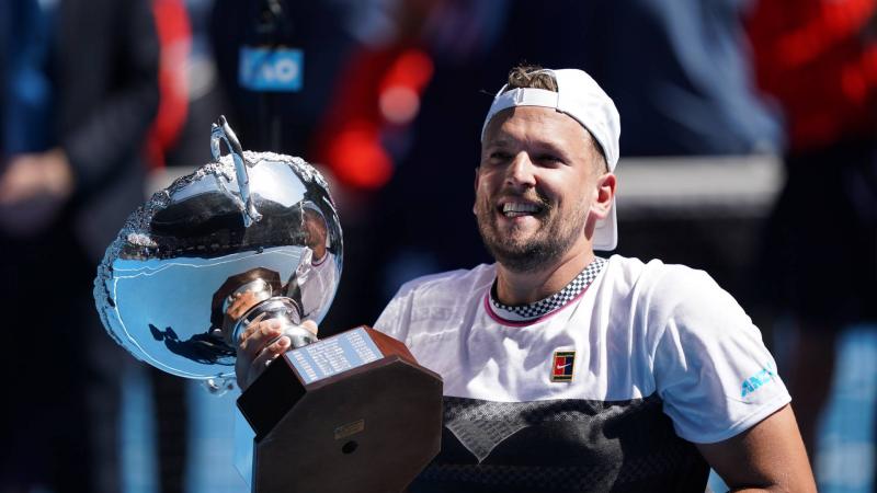 male wheelchair tennis player Dylan Alcott holds up a silver trophy and smiles