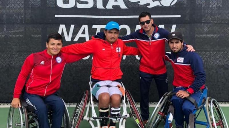 three male wheelchair tennis players and another man with their arms around eachother on a hard court