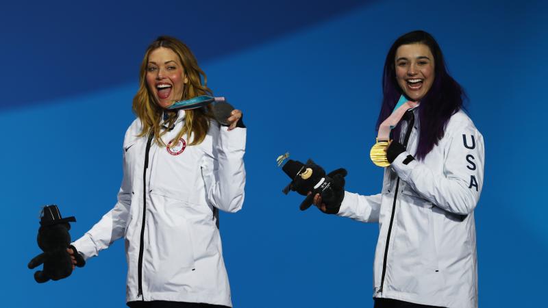 female Para snowboarders Amy Purdy and Brenna Huckaby holding up their medals and waving 