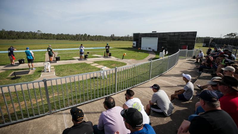 a wide shot of a sunny shooting range outside with athletes preparing to shoot
