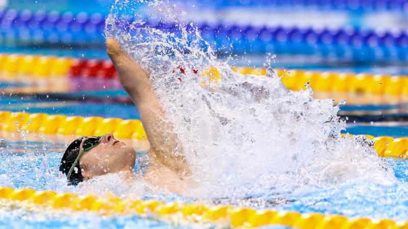 male Para swimmer Cameron Leslie lifts his arm up out of the water during a backstroke race