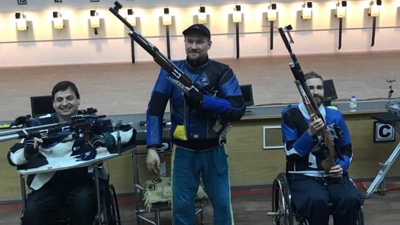 Three male medallists pose with their rifles 