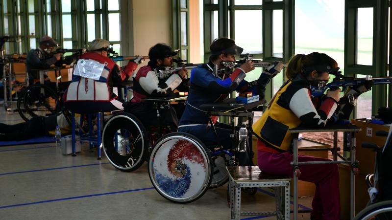 Para shooters sitting in wheelchairs firing rifles on the range