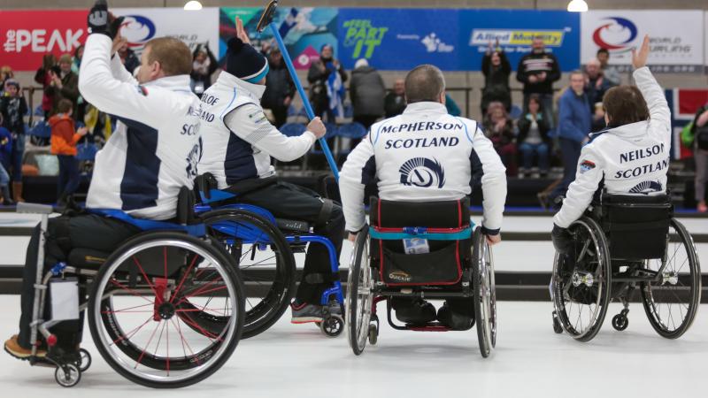 Four wheelchair curlers celebrating and waving to the crowd
