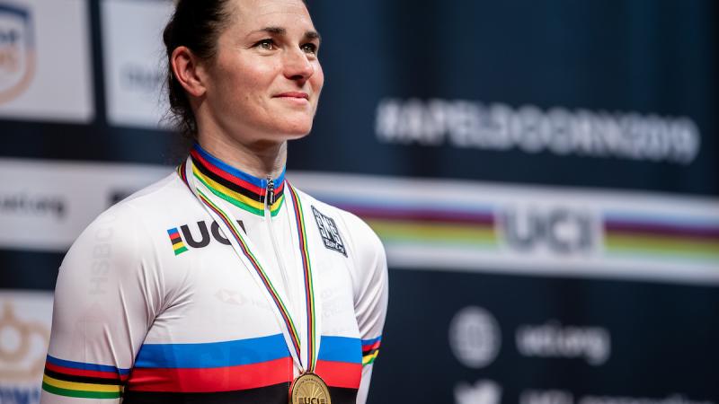 female Para cyclist Sarah Storey stands on the podium with a gold medal around her neck