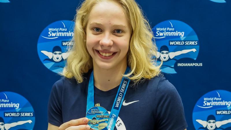 female Para swimmer Julia Gaffney smiles and holds up a gold medal
