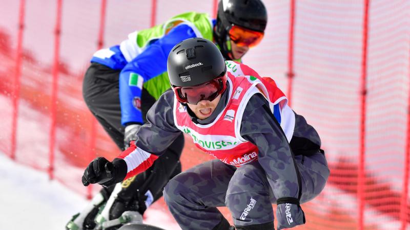 male Para snowboarder Patrick Mayrhofer rides in front of another snowboarder