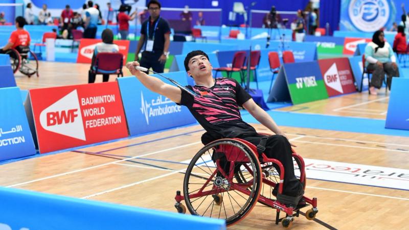 male Para badminton player Qu Zimao goes for a backhand shot on court